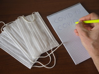 a man writes in a notebook COVID-19, near a medical mask