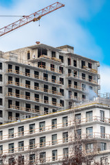 an apartment building under construction with a nearby high-rise crane.