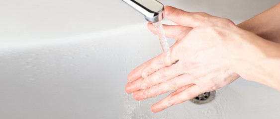  Washing hands under a stream of water  in the bathroom over the sink.  Panoramic banner background. Coronavirus, Covid-19