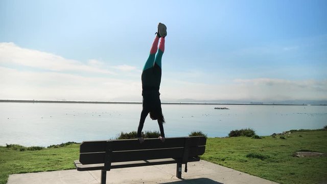 Young athletic girl does a handstand and split on back of park bench