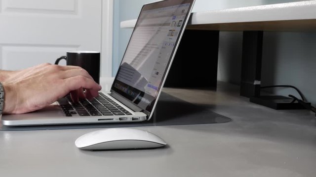 Caucasian male working from home on laptop and drinking coffee, closeup side view