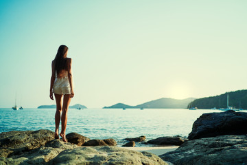 Fototapeta na wymiar Young woman with long hear standing on sea beach enjoying the view.