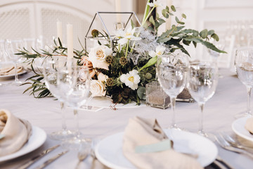 Wedding banquet. Celebratory tables with tablecloths are decorated with compositions of flowers, on the tables are plates with napkins, glasses and candles