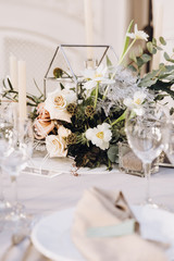 Wedding banquet. Celebratory tables with tablecloths are decorated with compositions of flowers, on the tables are plates with napkins, glasses and candles