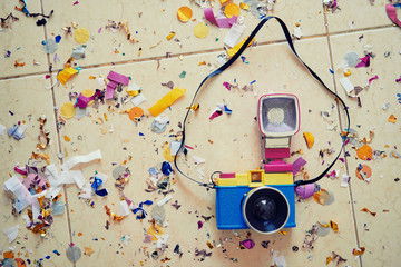 Party concept. Colorful photocamera laying on the floor covered with confetti.