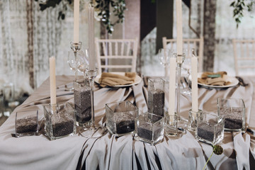 Wedding banquet. Celebratory tables with tablecloths are decorated with compositions of flowers, on the tables are plates with napkins, glasses and candles