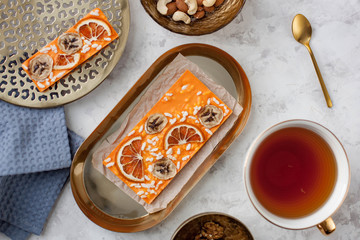 handmade orange chocolate bar with pieces of orange, banana and puffed rice lying on the table near a cup of tea