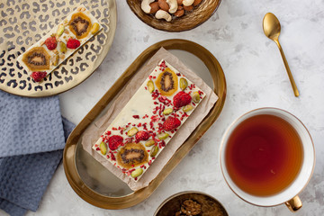 handmade white chocolate bar with kiwi, strawberry and pistachio lying on the table near a cup of tea