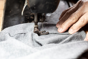 Senior woman's stitching grey fabric on vintage sewing machine, Thread, Needle, Close up shot, Selective focus, Sewing process, Female's hobby. Tailor concept