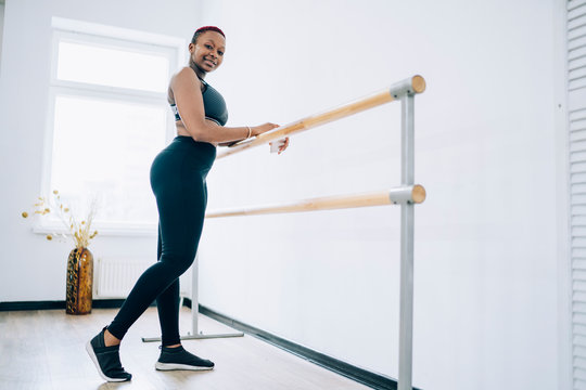 Smiling sportive female exercising on barre