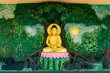 Batu, Indonesia - CIRCA Apr 2020: A meditating Buddha (under a tree) wall sculpture in Dhammadipa...