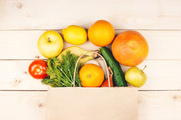 Paper shopping bag with organic vegetables and fruits flat lay on wooden background top view. Healthy food. Grocery store delivery, online supermarket concept. Web banner template. Stock photo.