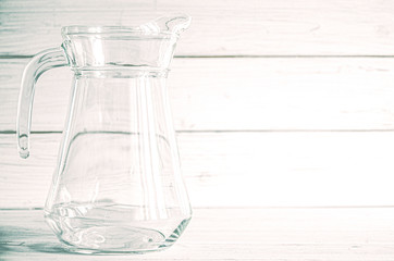 An empty glass carafe for water stands on a white wooden background