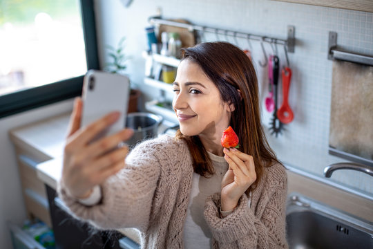 bella ragazza si fa un selfie in cucina mentre mangia una fragola