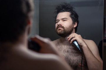 man shaves his beard in the reflection of the mirror