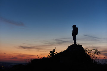Silhouette of astronaut standing on top of rocky hill with beautiful night sky on background. Space traveler wearing space suit with helmet. Concept of space travel. © anatoliy_gleb