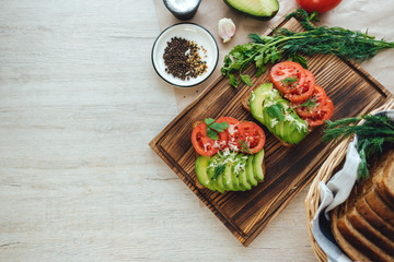 Fototapeta na wymiar Healthy vegan homemade sandwich, avocado and tomatoes with dark grain bread on a wooden board.