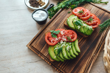 Healthy vegan homemade sandwich, avocado and tomatoes with dark grain bread on a wooden board.
