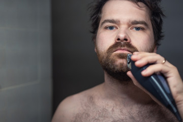 man shaves his beard in the reflection of the mirror