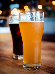 Two glasses of craft fresh brewed beer light and dark standing on a raw grungy wooden table with a blurred background with bokeh bubbles.