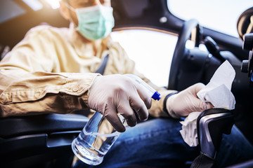 Man in protective suit with mask disinfecting inside car, wipe clean surfaces that are frequently touched, prevent infection of Covid-19 virus coronavirus,contamination of germs or bacteria. 