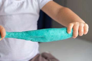 child preschooler stretches a turquoise dough for modeling. quarantine and self-isolation of children's creativity