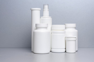 6 white jars for medicines and vitamins and dietary supplements without a name are on a gray shelf.