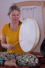 Close up of a woman in a yellow T-Shirt playing the gong drum in a yoga class.