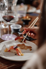 Girl eats sushi with Chinese chopsticks at a table in a restaurant. Close-up of hands. Soft focus