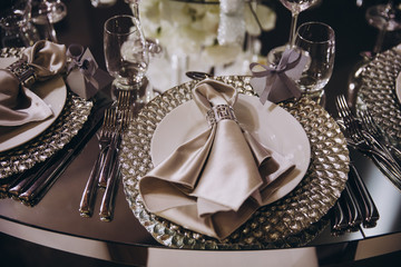 Stylish table setting. On the banquet table are plates with napkins, glasses and flower arrangements