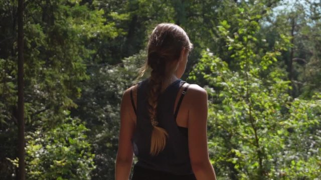Sporty young woman with long braided hair walking through forest on a sunny day