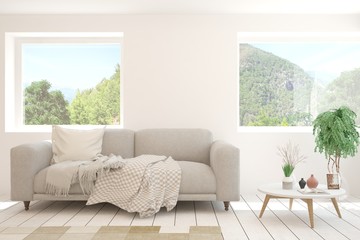 Fototapeta premium White living room with sofa and summer landscape in window. Scandinavian interior design. 3D illustration