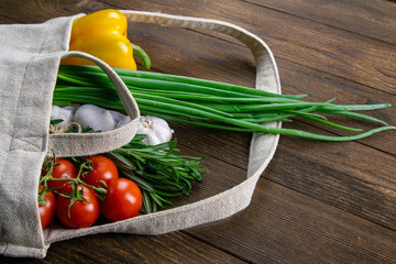 Woven bag of different health food on dark wooden table background. Green onion, garlic, tomato and...