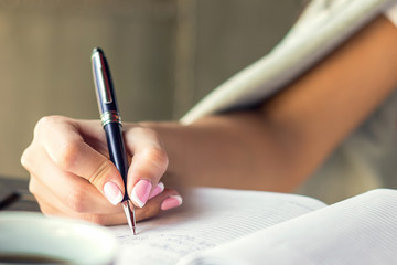 Business woman hand writing with pen in notepad at cafe.