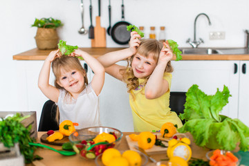 Beautiful chef sisters at kitchen preparing salad from colorful vegetables.