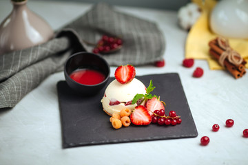 Appetizing sweet white round small cake with fresh berries and red sauce on a black stone board on a white background, horizontal