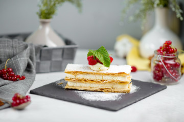 Side view on strawberry and whipped cream mille-feuille with fresh berries on a black stone board on the white background, horizontal
