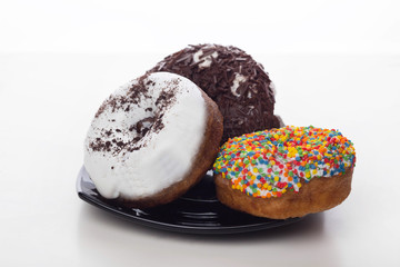 donuts with icing and chocolate in a plate on a white background