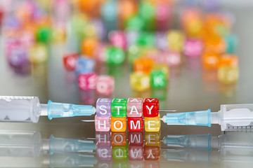 The inscription STAY HOME of multi-colored cubes on syringes needles. Concept of protection from covid-19. Quarantine during a coronavirus pandemic. Glass surface, closeup