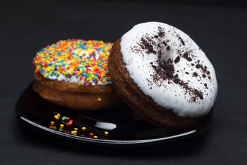 donuts with icing and chocolate in a plate on a dark background