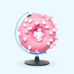 Pink sugarred donut with marshmallow as a globe on blue background. Negative space to insert your...