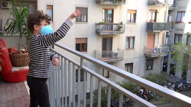 Europe, Italy , Milan - children boy  five years old with mask at home during quarantine due n-cov19 Coronavirus outbreak epidemic  - 
lifestyle and  play throwing paper airplanes from the balcony