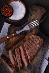 Sliced beef steak with knife and fork and spices on cutting board
