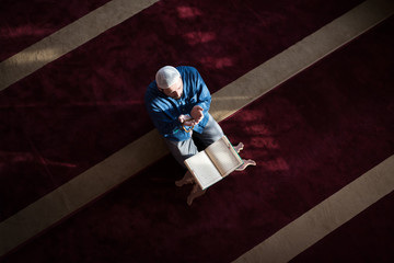 Young Arabic Muslim man reading Koran and praying. Religious muslim man reading holy koran inside...