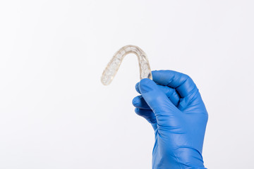 Férula dental para tratar el bruxismo sujeta con una mano con guante azul sobre un fondo blanco