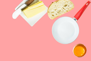 Breakfast ingredients butter slice of bread cracked raw egg frying pan on pink background. Culinary food poster with copy space