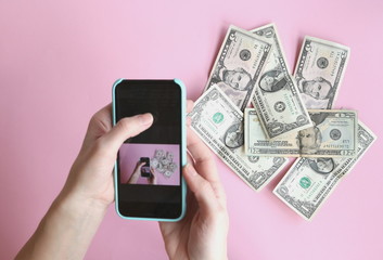 1, 5, 20 dollars are lying in a mess on a pink background, they are removed from the top of the smartphone, top view