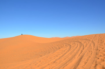 Fototapeta na wymiar Silhouette of a man sitting at the sand dunes. Merzouga is a small Moroccan town in the Sahara Desert, near the Algerian border. 