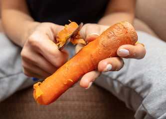 Girl peeling boiled carrots with a knife.