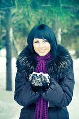 pretty woman in down-padded coat with fur collar holding snow in hands 